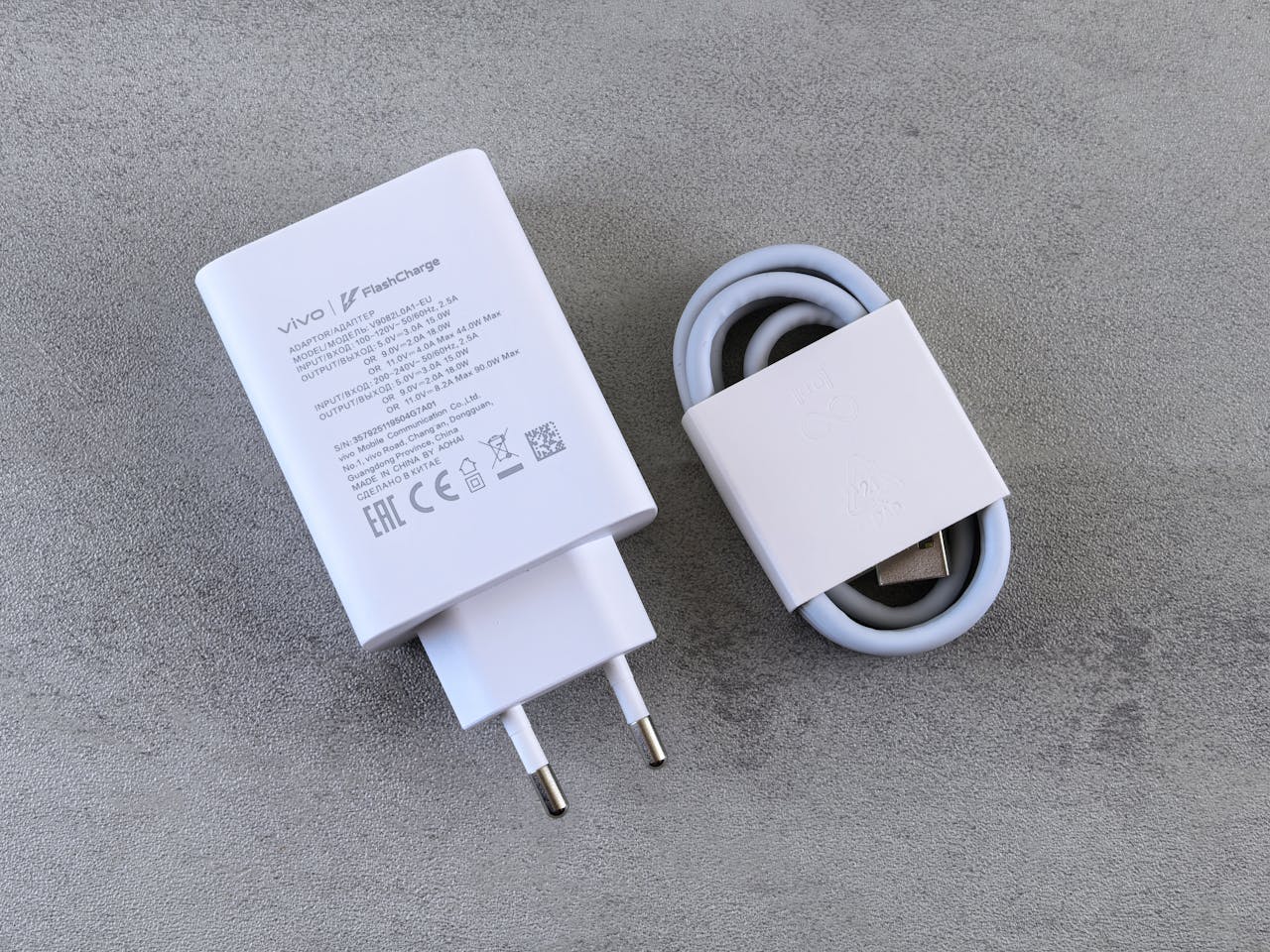 Close-up of Vivo FlashCharge adapter with cable on a textured concrete background, highlighting modern charging technology.